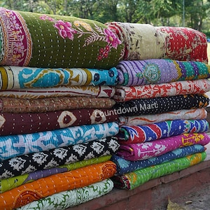 Könnte beinhalten: Ein Stapel bunter Kantha-Steppdecken, ein traditionelles indisches Textil, mit verschiedenen floralen und geometrischen Mustern. Die Decken sind gefaltet und übereinander gestapelt, was ein optisch ansprechendes Display ergibt.