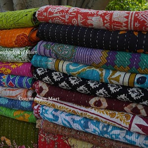 Puede incluir: Una pila de colchas kantha enrolladas, con varios colores y patrones. Las colchas muestran diseños en rojo, naranja, verde y azul. El texto "Countdown Mart" es visible en algunas colchas.