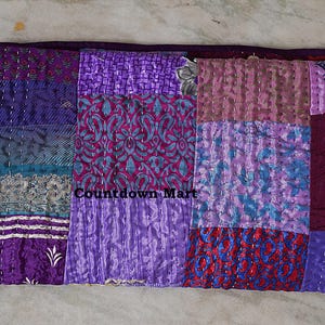 Könnte beinhalten: Ein Patchwork-Quilt in Lila-, Türkis- und Rottönen. Der Quilt besteht aus verschiedenen Stoffquadraten mit unterschiedlichen Mustern und Texturen, darunter Blumen- und geometrische Designs. Der Text "Countdown Mart" ist sichtbar.
