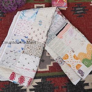 Könnte beinhalten: Eine gefaltete Patchwork-Quiltdecke mit verschiedenen floralen und geometrischen Mustern in Weiß, Creme und Pastelltönen. Die Quiltdecke zeigt verschiedene Abschnitte mit einzigartigen Designs. Der Text "Countdown Mart" ist sichtbar.