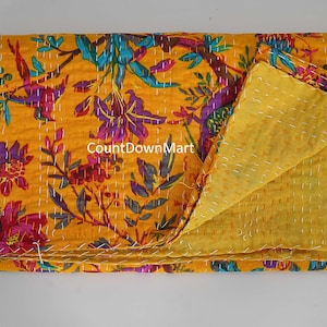 May include: A folded yellow floral quilt with a vibrant pattern of purple, blue, and red flowers and leaves. The quilt is made of a soft material and has a contrasting yellow backing. The stitching is visible throughout the quilt.