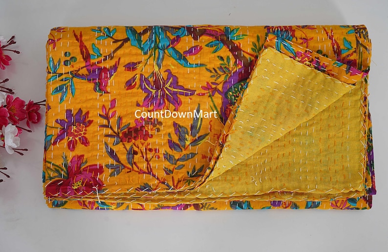 May include: A folded yellow floral quilt with a vibrant pattern of purple, blue, and red flowers and leaves. The quilt is made of a soft material and has a contrasting yellow backing. The stitching is visible throughout the quilt.