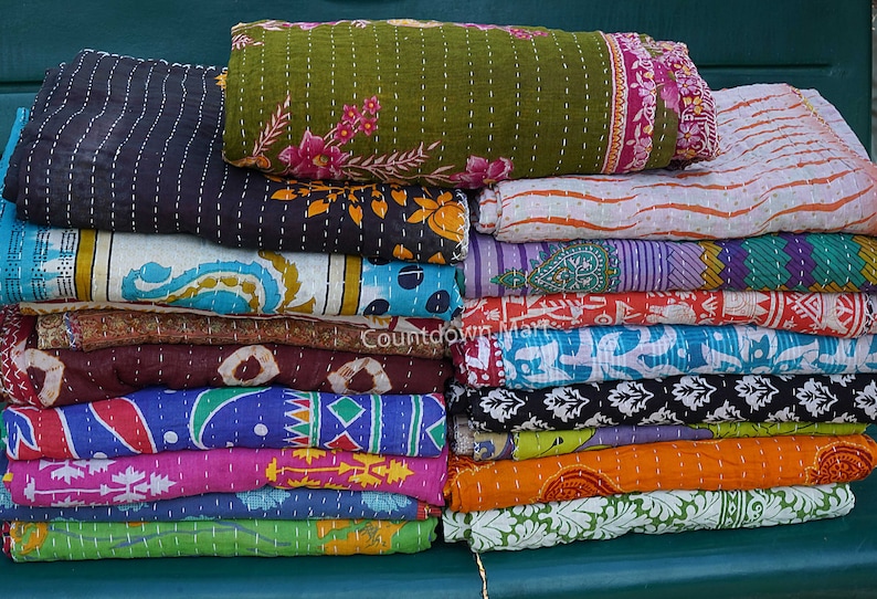 May include: A stack of colorful kantha quilts with various floral and geometric patterns. The quilts are made of recycled saris and are hand-stitched.