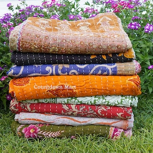 Könnte beinhalten: Ein Stapel bunter, gemusterter Quilts. Die Quilts sind in den Farbtönen Orange, Blau, Rot, Grün und Braun gehalten. Die Quilts haben ein gesticktes Design und sind übereinander gestapelt. Der Text "Countdown Mart" ist auf einem der Quilts zu sehen.