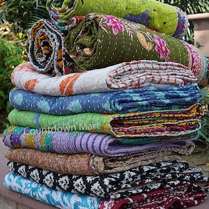 May include: A stack of colorful kantha quilts, a traditional Indian textile, with various floral and geometric patterns. The quilts are rolled up and stacked on top of each other, creating a visually appealing display.