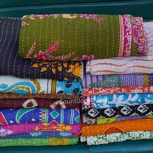 Könnte beinhalten: Ein Stapel bunter, gemusterter Kantha-Quilts. Die Quilts weisen verschiedene Designs auf, darunter florale, geometrische und abstrakte Muster in Grün-, Blau-, Orange- und Lilatönen. Jeder Quilt ist gefaltet und gestapelt, was die aufwendigen Nähte zeigt.