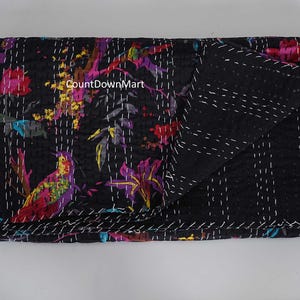 May include: Black quilt with a vibrant floral and bird pattern in shades of pink, purple, yellow, and teal. The quilt is hand-stitched with white thread, and the folded edge reveals a solid black reverse side.