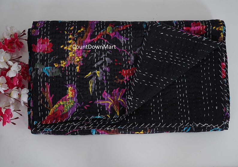 May include: Black quilt with a vibrant floral and bird pattern in shades of pink, purple, yellow, and teal. The quilt is hand-stitched with white thread, and the folded edge reveals a solid black reverse side.