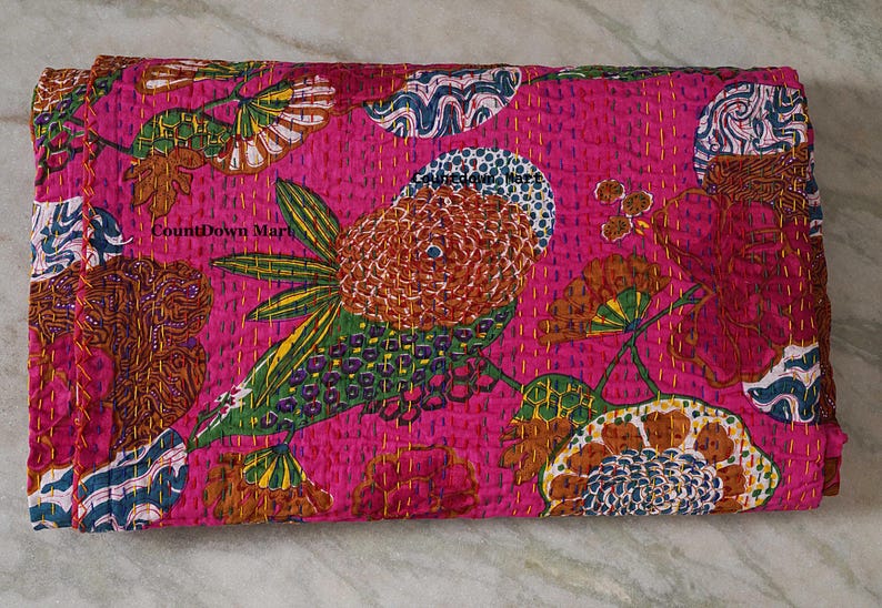 May include: A folded, hot pink quilt with a large, colorful floral design. The design includes a large, stylized flower with brown, green, and white details. The quilt is stitched with yellow thread, and the text "CountDown Mart" is visible.
