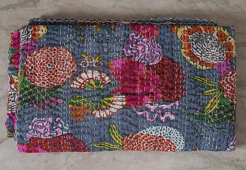 May include: A folded, floral-patterned quilt in shades of gray, pink, orange, and green. The quilt features large, stylized flower designs and is stitched with white thread. The text "Countdown Mart" is visible on the quilt.