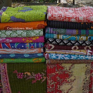 May include: A stack of colorful, patterned quilts. The quilts feature various designs, including floral and geometric patterns, in shades of green, orange, pink, blue, and red. The text "Countdown Mart" is visible on one of the quilts.