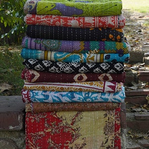 May include: A stack of colorful kantha quilts, a traditional Indian textile, with intricate patterns and stitching. The quilts are made from recycled saris and are known for their durability and beauty.
