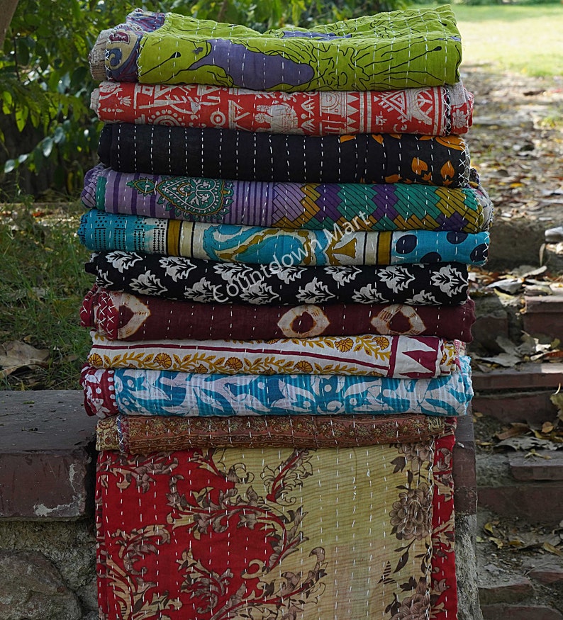 May include: A stack of colorful kantha quilts, a traditional Indian textile, with intricate patterns and stitching. The quilts are made from recycled saris and are known for their durability and beauty.