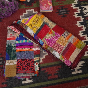 Könnte beinhalten: Ein Patchwork-Quilt mit einer Vielzahl von bunten Stoffquadraten. Der Quilt zeigt rote, gelbe, blaue und gemusterte Stoffe. Die Ränder sind dunkelburgunderfarben. Der Text "Countdown Martin" ist sichtbar. Ein Buch und Blumen sind im Hintergrund.