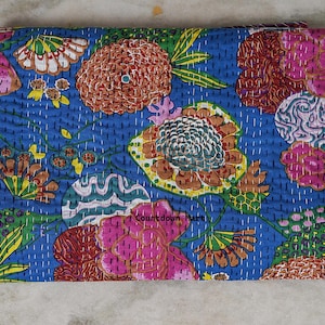 May include: A folded blue textile with a floral pattern. The design features large flowers in shades of pink, orange, and yellow, with green leaves and white stitching. The textile is likely a quilt or blanket.