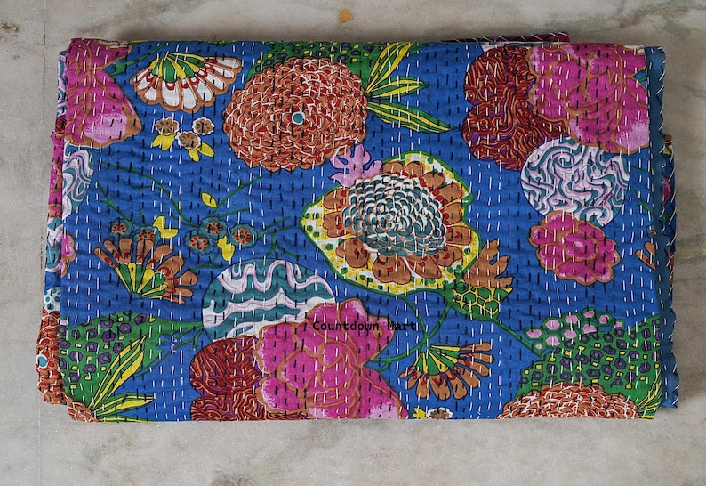 May include: A folded blue textile with a floral pattern. The design features large flowers in shades of pink, orange, and yellow, with green leaves and white stitching. The textile is likely a quilt or blanket.