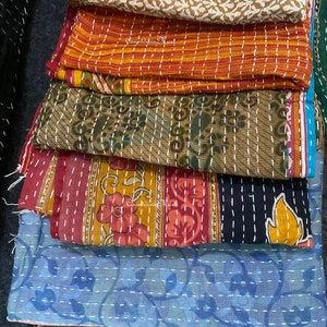 May include: A stack of colorful kantha quilts with intricate embroidery and stitching. The quilts are made from recycled saris and feature a variety of floral and geometric patterns.