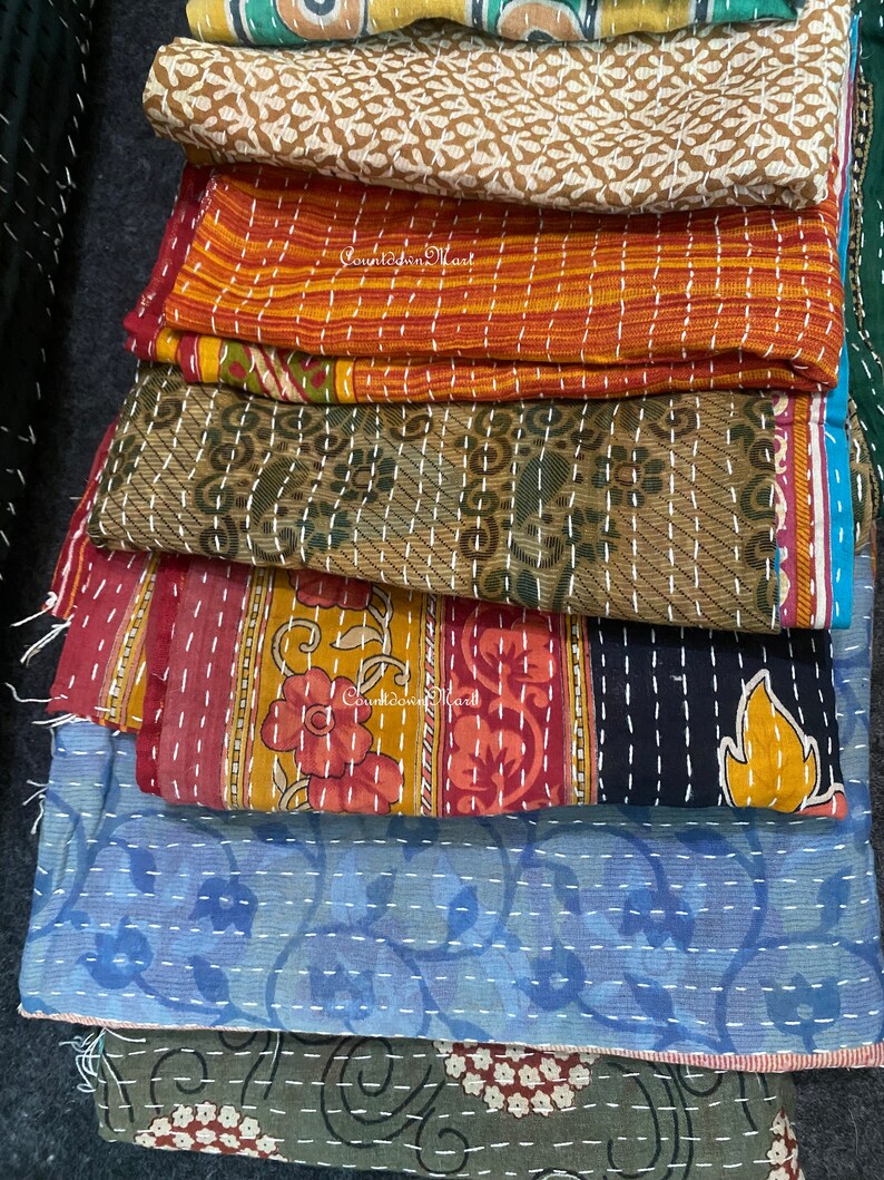 May include: A stack of colorful kantha quilts with intricate embroidery and stitching. The quilts are made from recycled saris and feature a variety of floral and geometric patterns.