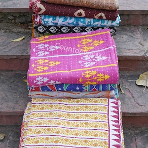 May include: A stack of colorful kantha quilts with various floral and geometric patterns. The quilts are made of cotton and are hand-stitched. The quilts are folded and stacked on top of each other, creating a visually appealing display.