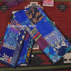 Könnte beinhalten: Eine gefaltete Patchwork-Steppdecke mit einer Vielzahl von blauen, marinefarbenen und gemusterten Stoffen. Die Steppdecke weist Blumen- und Paisley-Designs auf, mit dem Text "Countdown Mart" sichtbar. Die Steppdecke liegt auf einem rot-schwarz gemusterten Teppich.