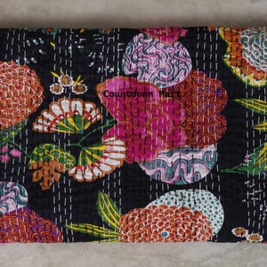 May include: A folded, black floral quilt with a vibrant pattern. The design features large, stylized flowers in shades of orange, pink, green, and white, stitched onto the fabric. The text "Countdown Mart" is visible on the quilt.