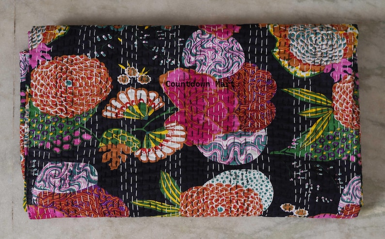 May include: A folded, black floral quilt with a vibrant pattern. The design features large, stylized flowers in shades of orange, pink, green, and white, stitched onto the fabric. The text "Countdown Mart" is visible on the quilt.