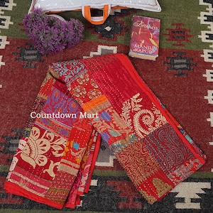 Könnte beinhalten: Ein roter Patchwork-Quilt mit verschiedenen Mustern und Texturen. Der Quilt ist gefaltet und zeigt verschiedene Abschnitte mit floralen und geometrischen Designs. Der Text "Countdown Mart" ist sichtbar. Ein Buch und lila Blumen sind ebenfalls vorhanden.
