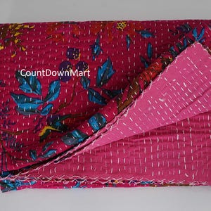 May include: A folded, reversible quilt with a magenta floral pattern on one side and a solid magenta color on the other. The quilt features white stitching and the text "CountDownMart".
