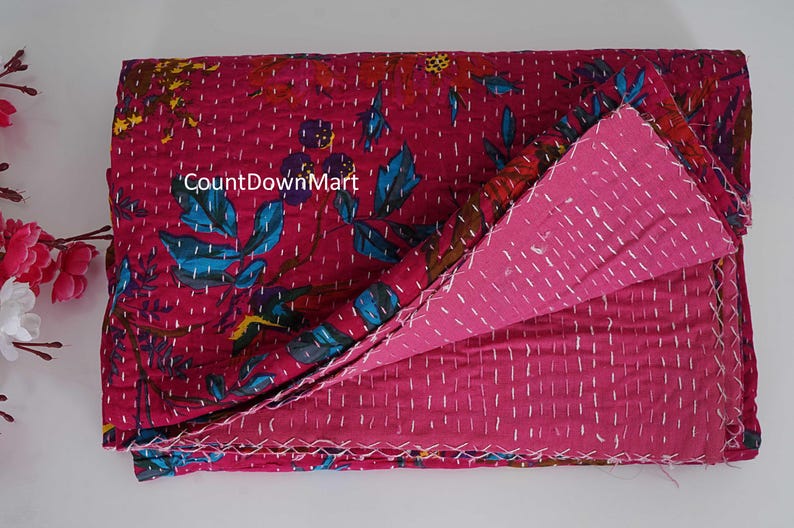 May include: A folded, reversible quilt with a magenta floral pattern on one side and a solid magenta color on the other. The quilt features white stitching and the text "CountDownMart".