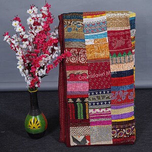 May include: A patchwork quilt with a variety of colors and patterns, including red, blue, green, and yellow. The quilt is made of recycled saris and has a burgundy border. The text "Countdown Mart" is visible in the center of the quilt.
