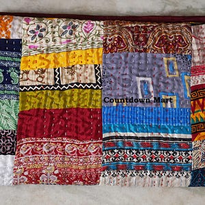 Könnte beinhalten: Ein Patchwork-Quilt mit einer Vielzahl von bunten Stoffquadraten. Der Quilt weist eine Mischung aus Mustern auf, darunter Blumen-, Paisley- und geometrische Designs. Der Text "Countdown Mart" ist auf dem Quilt sichtbar. Die Ränder sind einfarbig kastanienbraun.