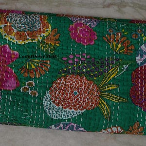 May include: A folded green textile with a vibrant floral pattern. The design features large, stylized flowers in shades of pink, orange, and yellow, with white stitching. The textile is likely a quilt or blanket.