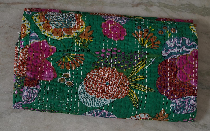 May include: A folded green textile with a vibrant floral pattern. The design features large, stylized flowers in shades of pink, orange, and yellow, with white stitching. The textile is likely a quilt or blanket.
