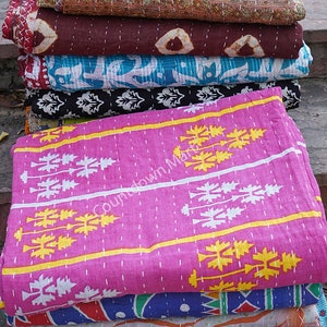 May include: A stack of colorful kantha quilts with various patterns, including floral, geometric, and paisley designs. The quilts are made of cotton and are hand-stitched. The top quilt is pink with white and yellow geometric patterns.