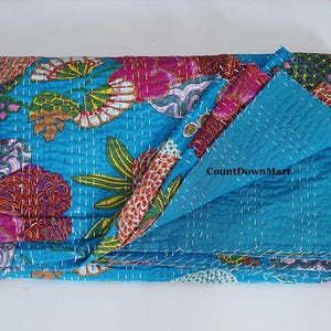 May include: A folded, turquoise quilt with a floral pattern in pink, orange, and green. The quilt is hand-stitched with white thread. The text "CountDownMart" is visible on the quilt. The quilt is folded on a white surface.