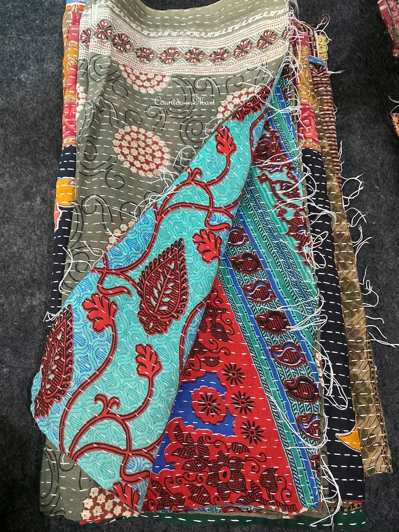 May include: A multi-colored kantha quilt made from recycled saris. The quilt features a variety of floral and paisley patterns in shades of blue, green, red, and black. The quilt is hand-stitched and has a unique, vintage look.