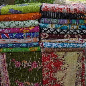 May include: A stack of colorful kantha quilts with various floral and geometric patterns. The quilts are made of cotton and are hand-stitched. They are perfect for adding a touch of bohemian style to any room.