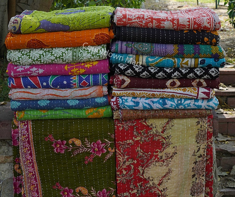 May include: A stack of colorful kantha quilts with various floral and geometric patterns. The quilts are made of cotton and are hand-stitched. They are perfect for adding a touch of bohemian style to any room.