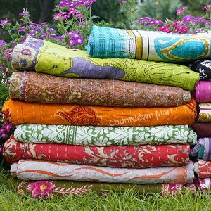 Könnte beinhalten: Ein Stapel gerollter Quilts in leuchtenden Farben, darunter Grün, Orange und Rot, mit floralen und geometrischen Mustern. Die Quilts zeigen eine Vielzahl von Designs. Der Text "Countdown Mart" ist auf einem der Quilts zu sehen.