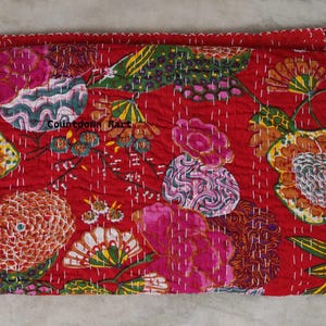 May include: A folded red textile with a floral pattern. The design features large flowers in shades of pink, orange, and yellow, with green leaves. The stitching is white, and the textile has a quilted appearance. The text "Countdown Mart" is visible.