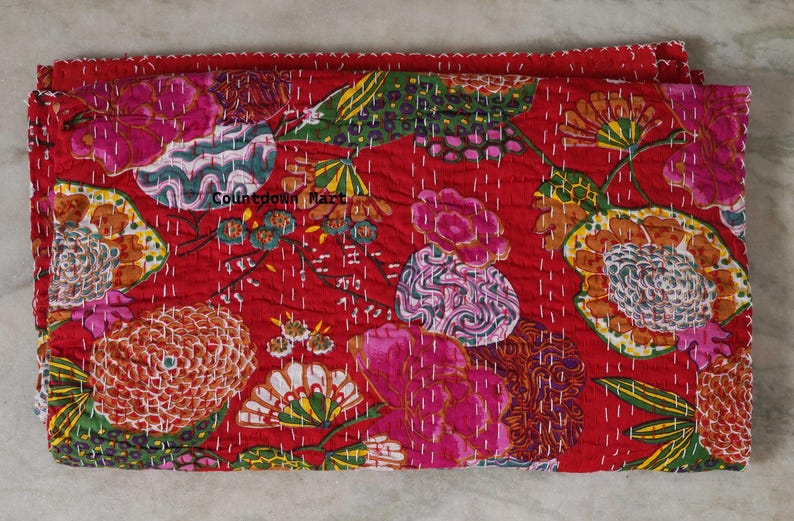 May include: A folded red textile with a floral pattern. The design features large flowers in shades of pink, orange, and yellow, with green leaves. The stitching is white, and the textile has a quilted appearance. The text "Countdown Mart" is visible.