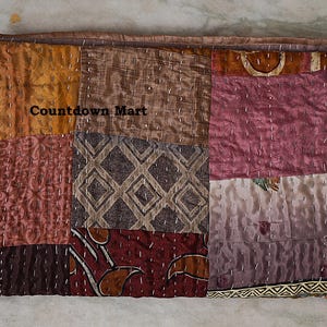 Könnte beinhalten: Ein Patchwork-Textil mit verschiedenen Farben und Mustern. Es besteht aus rechteckigen Teilen in Orange-, Braun- und Lilatönen. Der Text "Countdown Mart" ist sichtbar. Die Teile sind mit weißem Faden zusammengenäht.