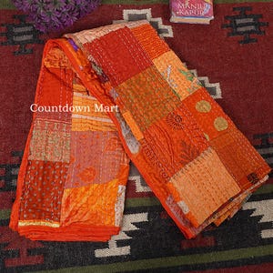 Könnte beinhalten: Eine orangefarbene Patchwork-Steppdecke mit einer Vielzahl von Mustern und Texturen. Die Steppdecke besteht aus verschiedenen Stoffen, die mit weißem Faden zusammengenäht sind. Der Text "Countdown Mart" ist auf der Steppdecke zu sehen.