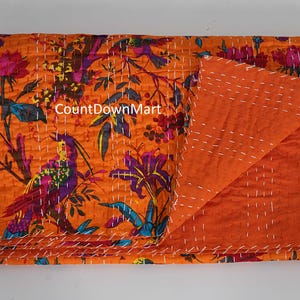 May include: An orange kantha quilt with a floral and bird pattern. The quilt features a vibrant design with purple, blue, and pink accents. The reverse side is a solid orange color, and the quilt is stitched with white thread. The text "CountDownMart" is visible.