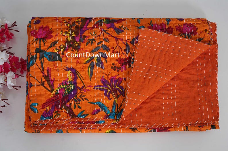 May include: An orange kantha quilt with a floral and bird pattern. The quilt features a vibrant design with purple, blue, and pink accents. The reverse side is a solid orange color, and the quilt is stitched with white thread. The text "CountDownMart" is visible.