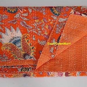 Peut inclure: Une courtepointe orange avec un motif floral dans les tons de bleu, blanc, jaune et rouge. La courtepointe est pli&eacute;e pour r&eacute;v&eacute;ler le dessous orange uni et pr&eacute;sente des coutures blanches. Le texte "CountDownMart" est visible.