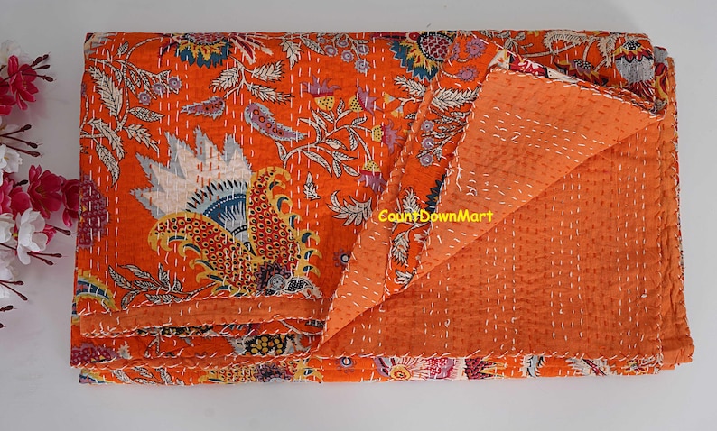 Peut inclure: Une courtepointe orange avec un motif floral dans les tons de bleu, blanc, jaune et rouge. La courtepointe est pli&eacute;e pour r&eacute;v&eacute;ler le dessous orange uni et pr&eacute;sente des coutures blanches. Le texte "CountDownMart" est visible.