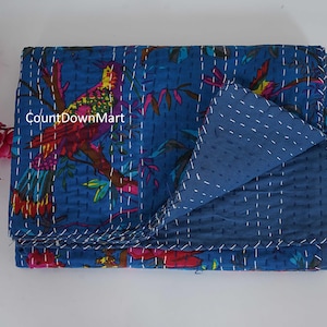 May include: A folded blue quilt with a colorful bird and floral design. The bird is perched on a branch with red, yellow, and green feathers. The quilt is stitched with white thread and has a solid blue reverse side. The text "CountDownMart" is visible.