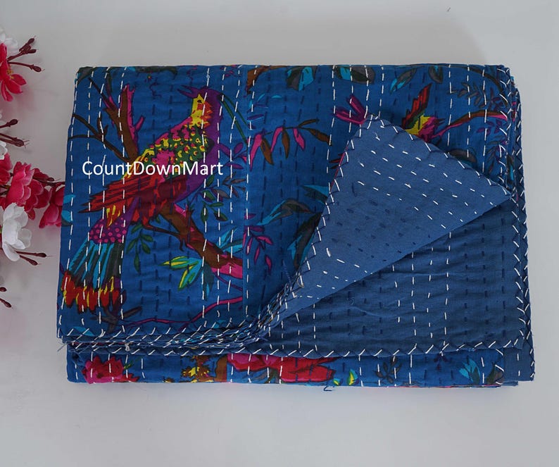 May include: A folded blue quilt with a colorful bird and floral design. The bird is perched on a branch with red, yellow, and green feathers. The quilt is stitched with white thread and has a solid blue reverse side. The text "CountDownMart" is visible.