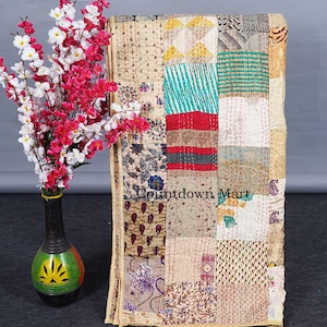 Könnte beinhalten: Ein Patchwork-Quilt mit verschiedenen gemusterten Stoffen in Beige, Rot, Türkis und floralen Designs. Der Quilt wird neben einer Vase mit rosa und weißen Blumen präsentiert. Der Text "Countdown Mart" ist auf dem Quilt zu sehen.